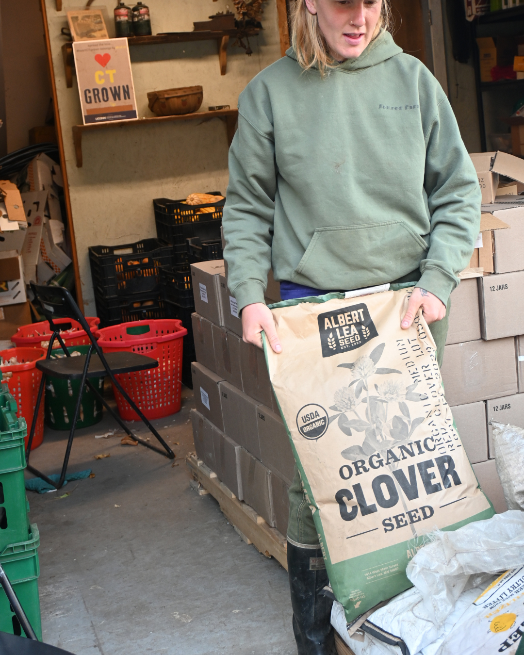 woman holding a large bag of clover seed on top of other seed bags