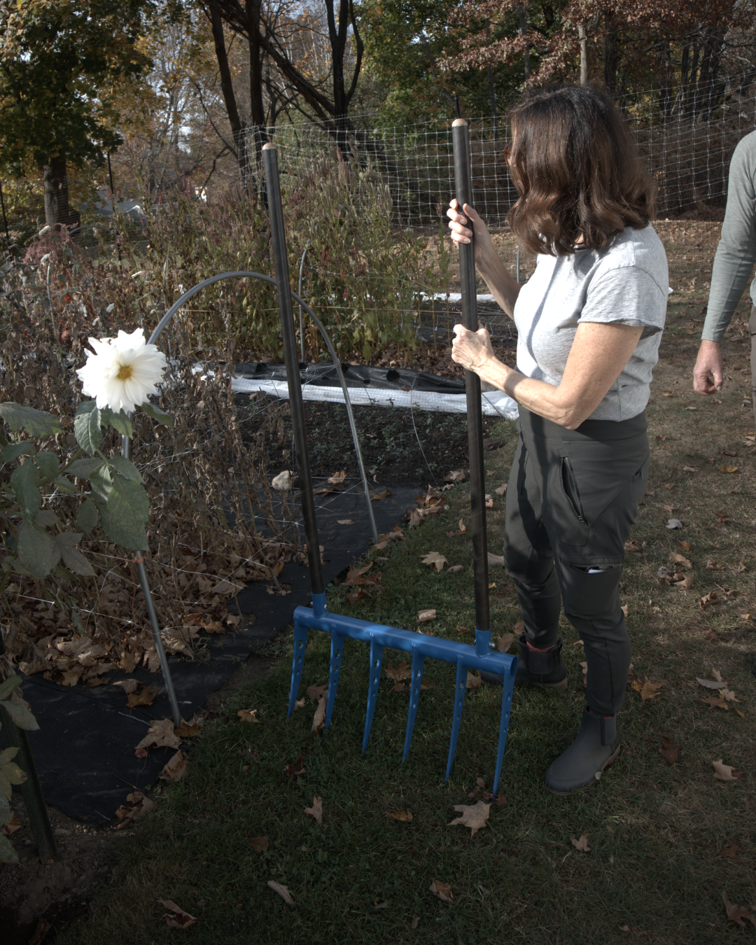 Woman holding a broadfork in front of her growing space