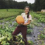 Nicole, smiling, holding a big pumpkin in a field